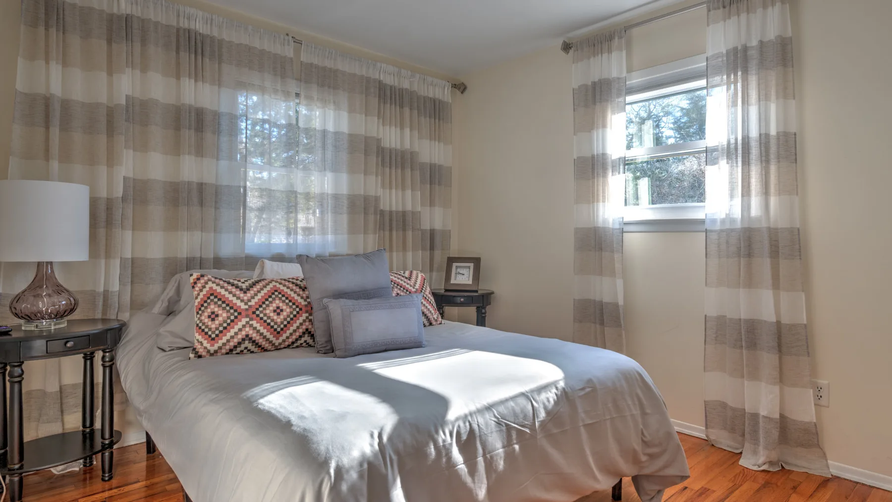 A bedroom with a bed, patterned curtains, and two windows.