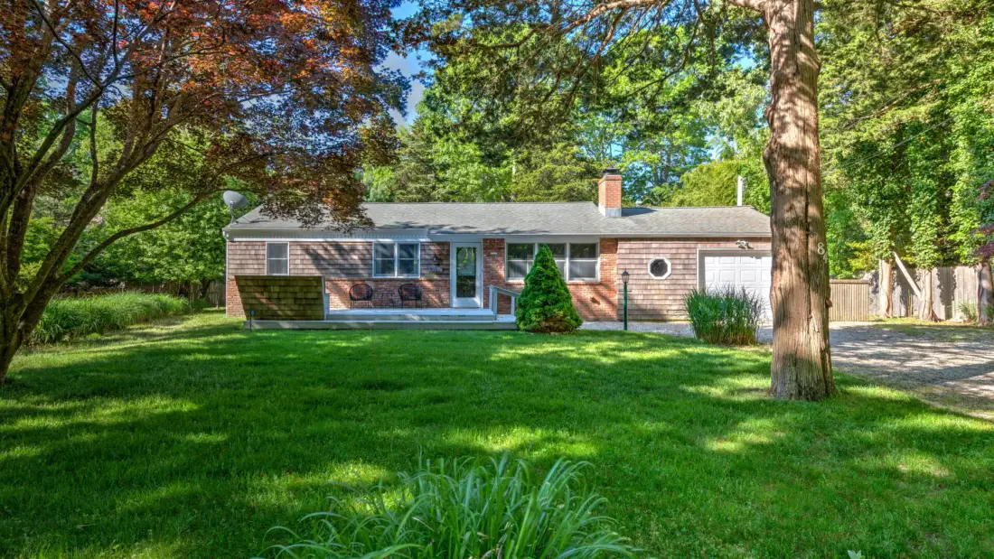 A brick house sits behind a broad green lawn and mature trees.