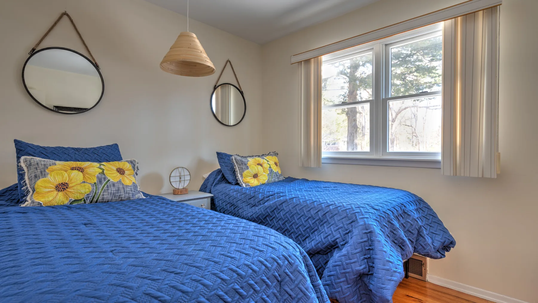 A bedroom with two beds covered in blue bedding beside a window.