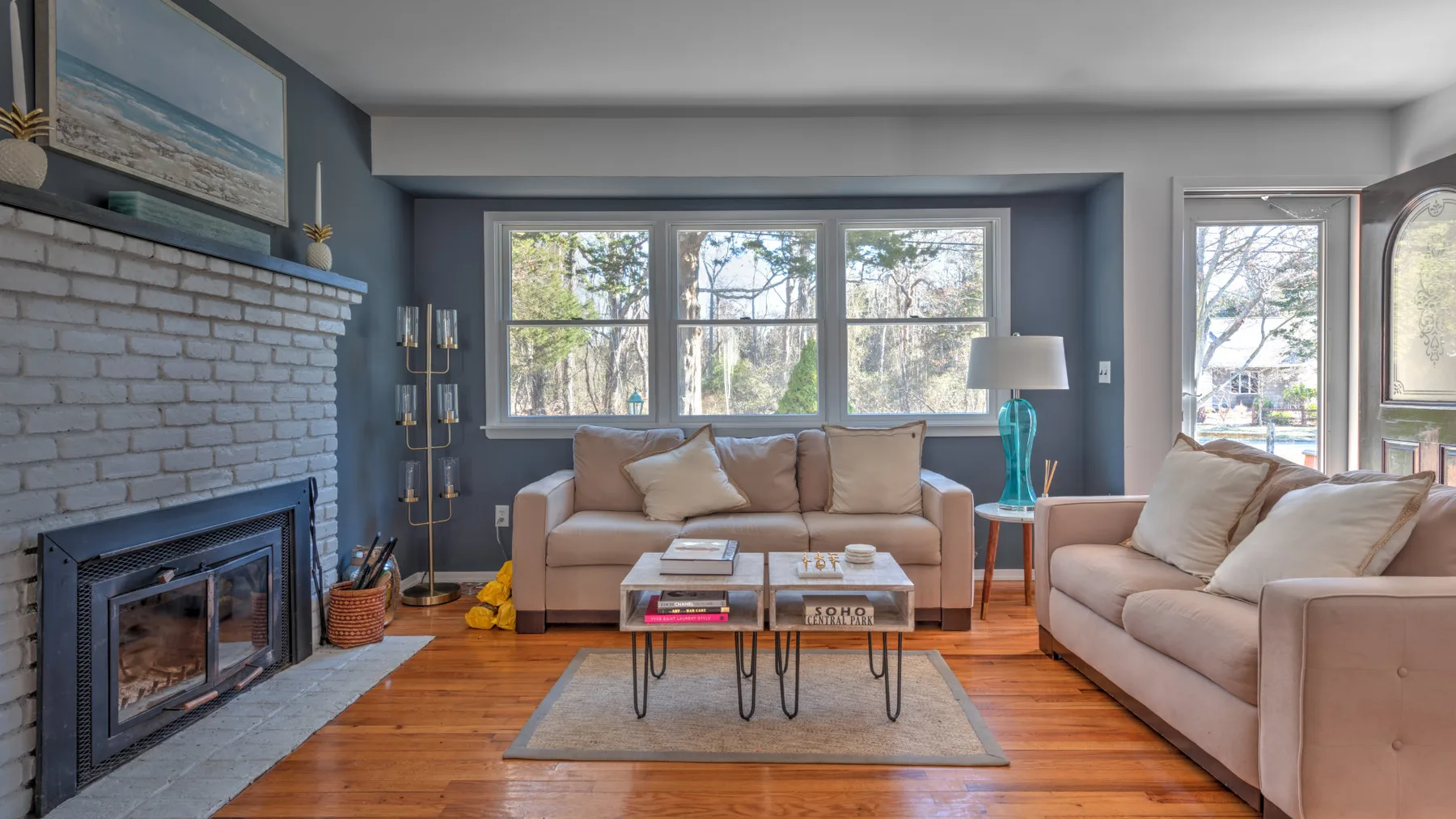 A living room with sofas, a fireplace, and large windows overlooking trees.