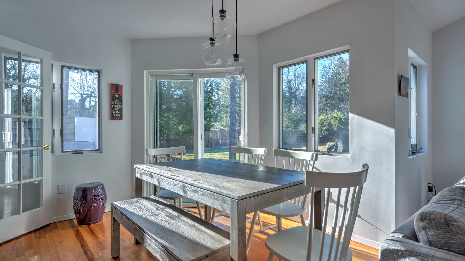 A bright dining area features a long table beside large windows and a glass door.