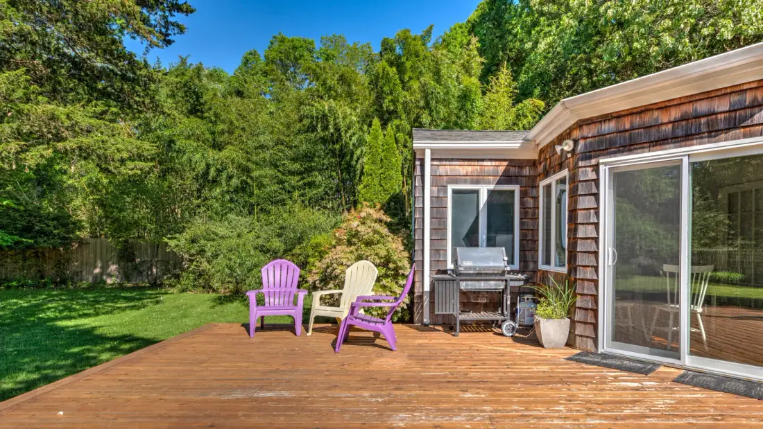 A wooden deck beside a house, with colorful seating and a wooded yard.