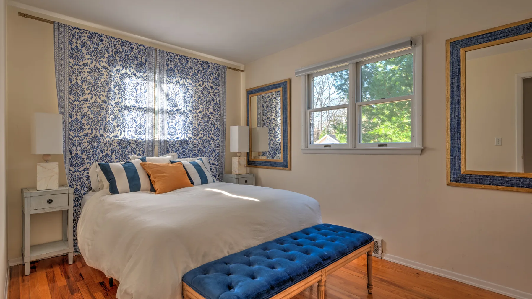 A bedroom with a bed, patterned curtains, and a blue bench at its foot.