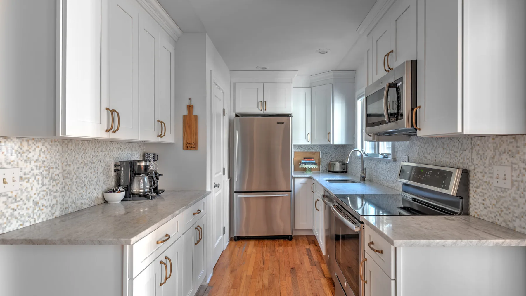 A bright kitchen with white cabinetry, stainless steel appliances, and wood flooring.