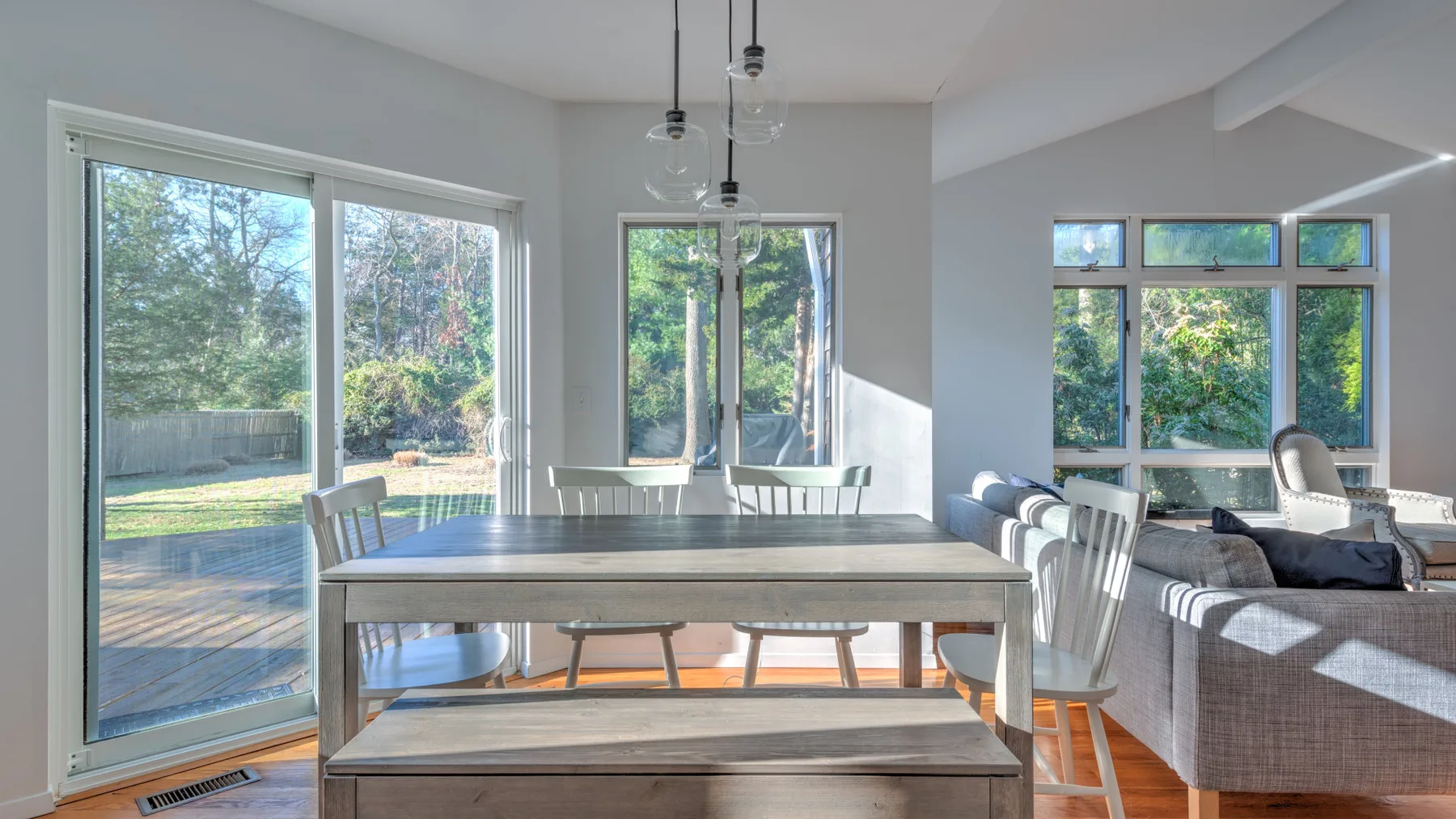 A bright open-plan dining and living area has large windows and a long dining table.