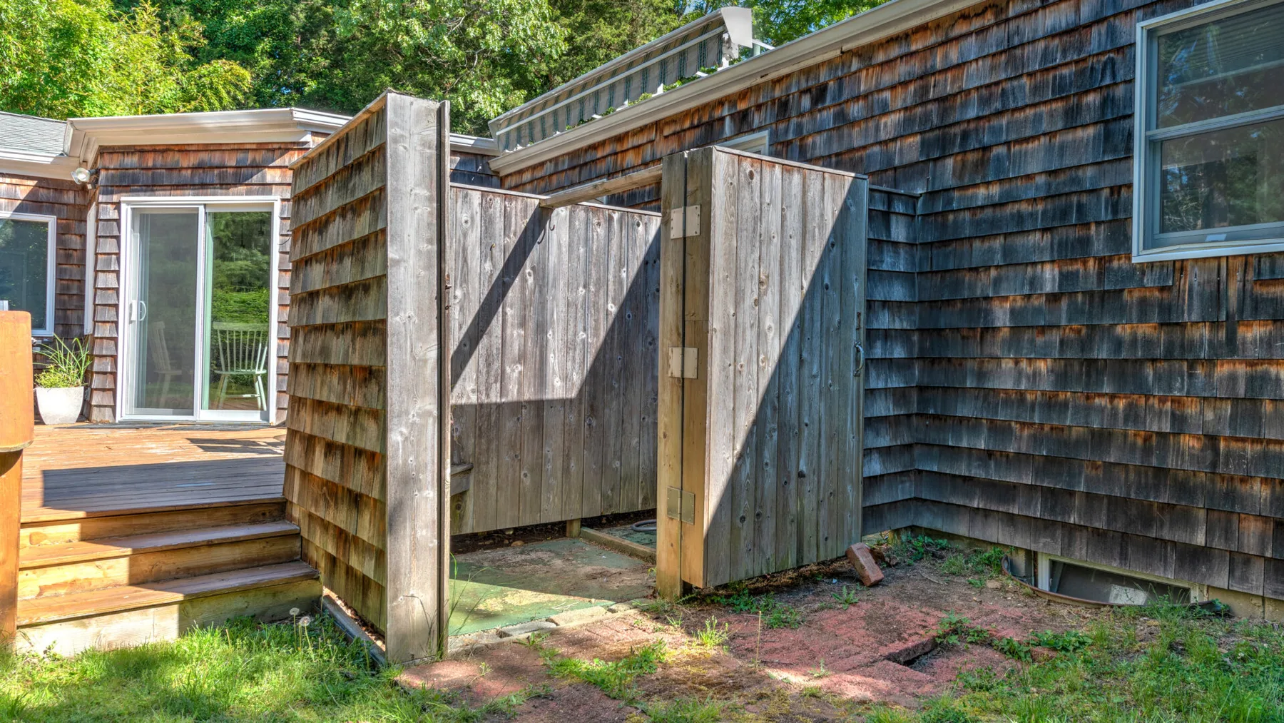 A wooden outdoor area with a raised deck and privacy screens beside a shingled building.