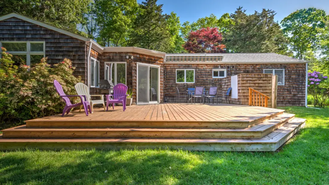 A wooden deck with outdoor seating extends along a shingled house.