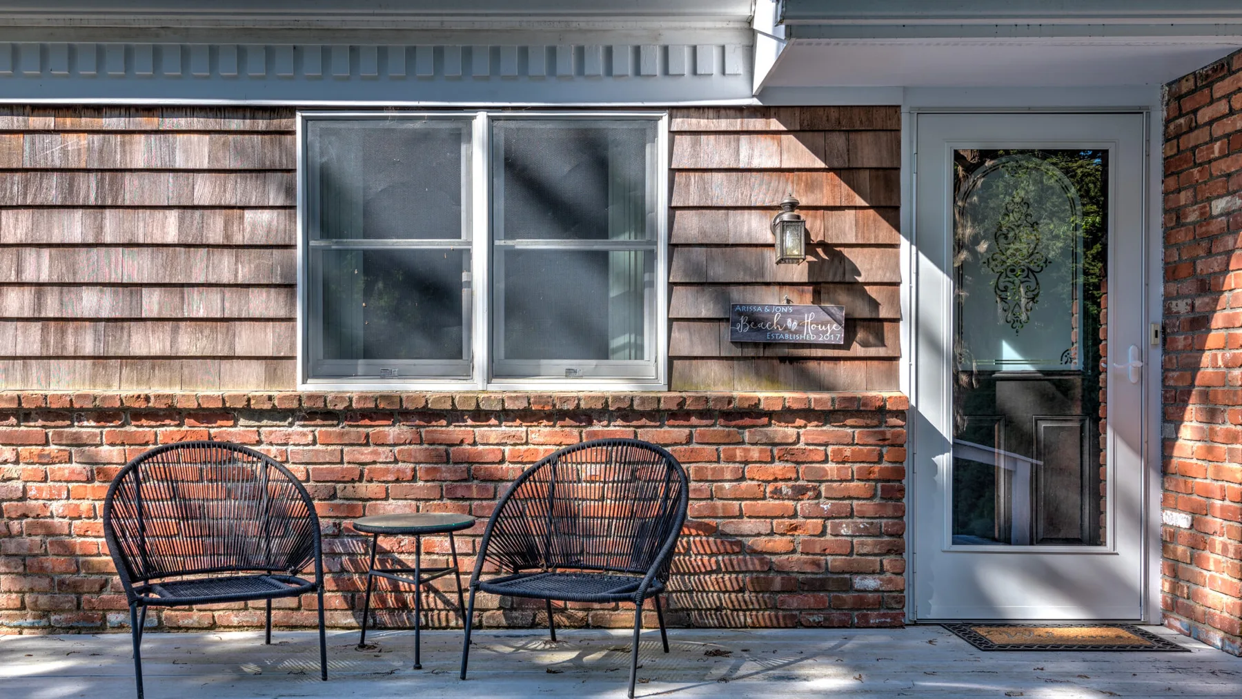 A brick-front entrance with a glass door, window, and two outdoor seats.