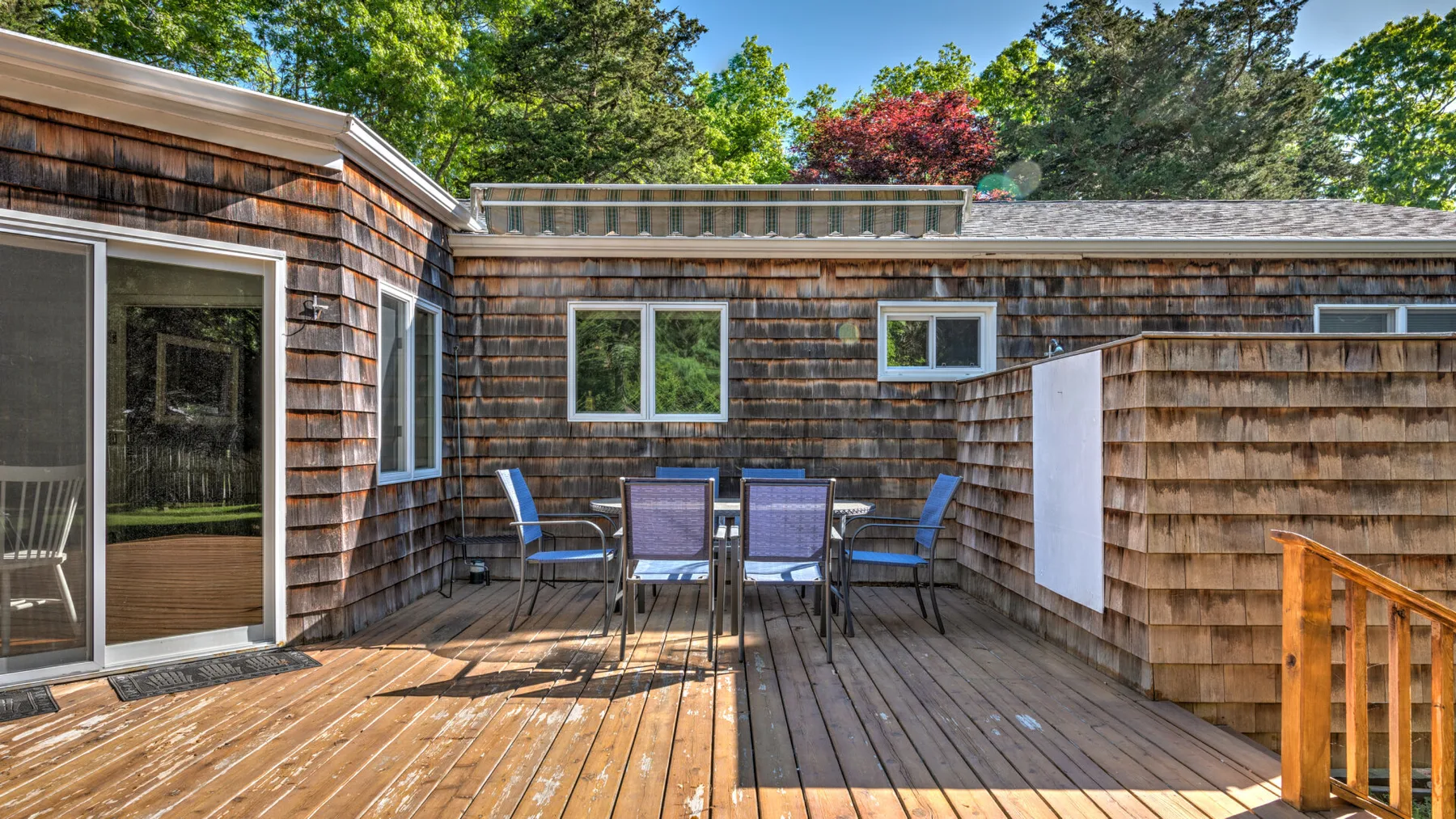 A wooden deck with outdoor seating sits beside a shingled building.