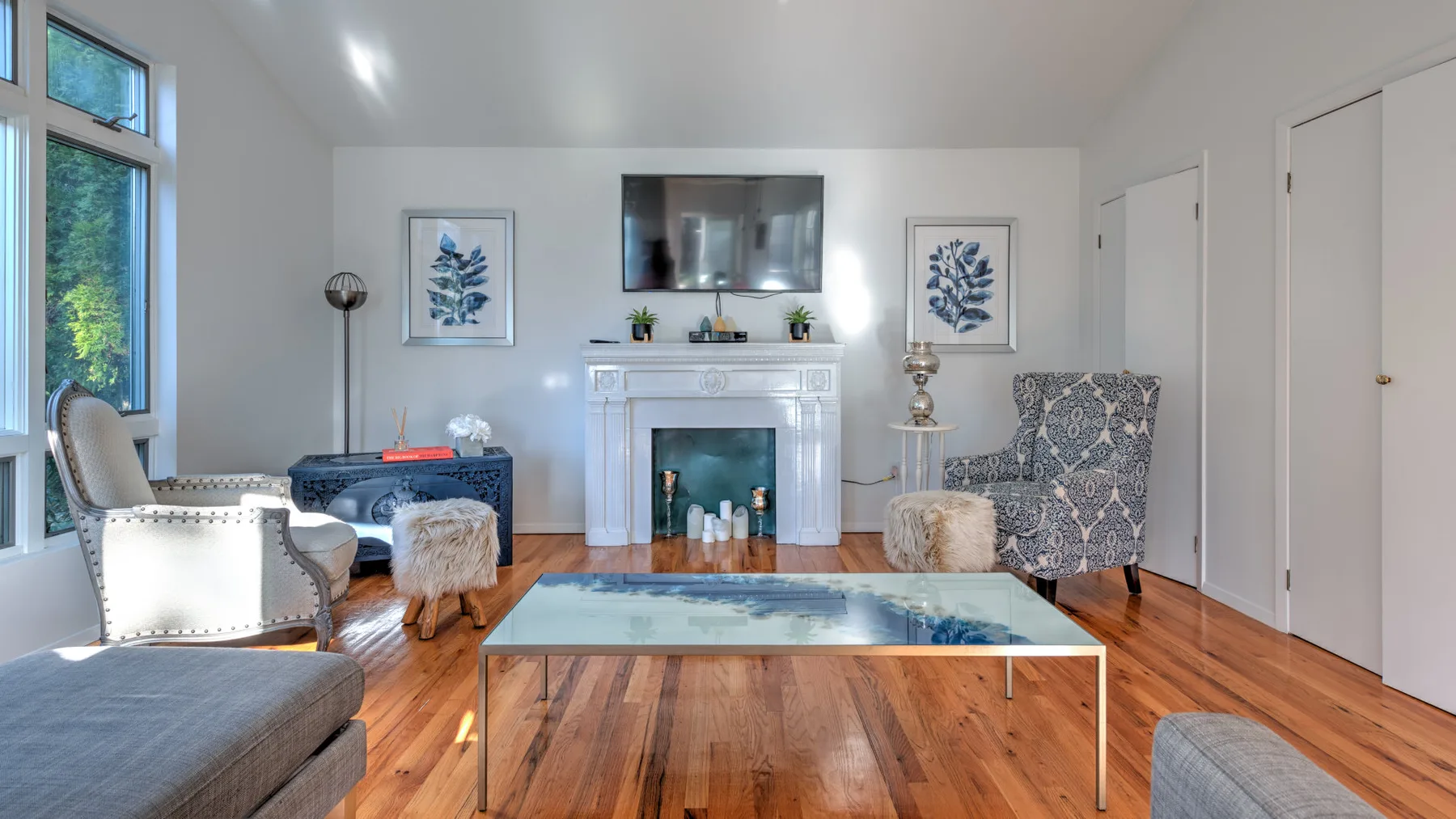 A bright living room with seating arranged around a fireplace and glass coffee table.