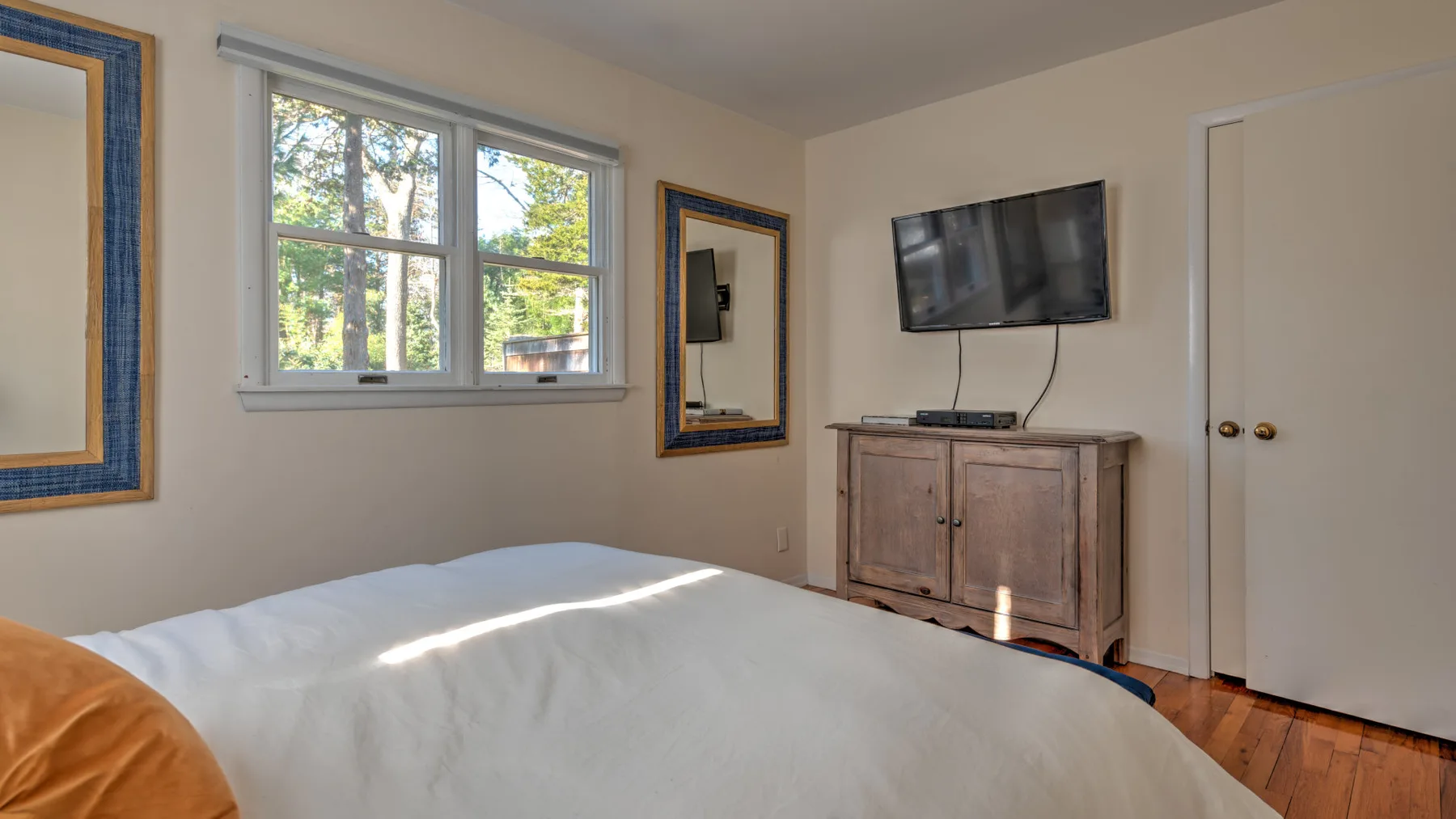 A bedroom with a bed, a window, and a television above a wooden cabinet.