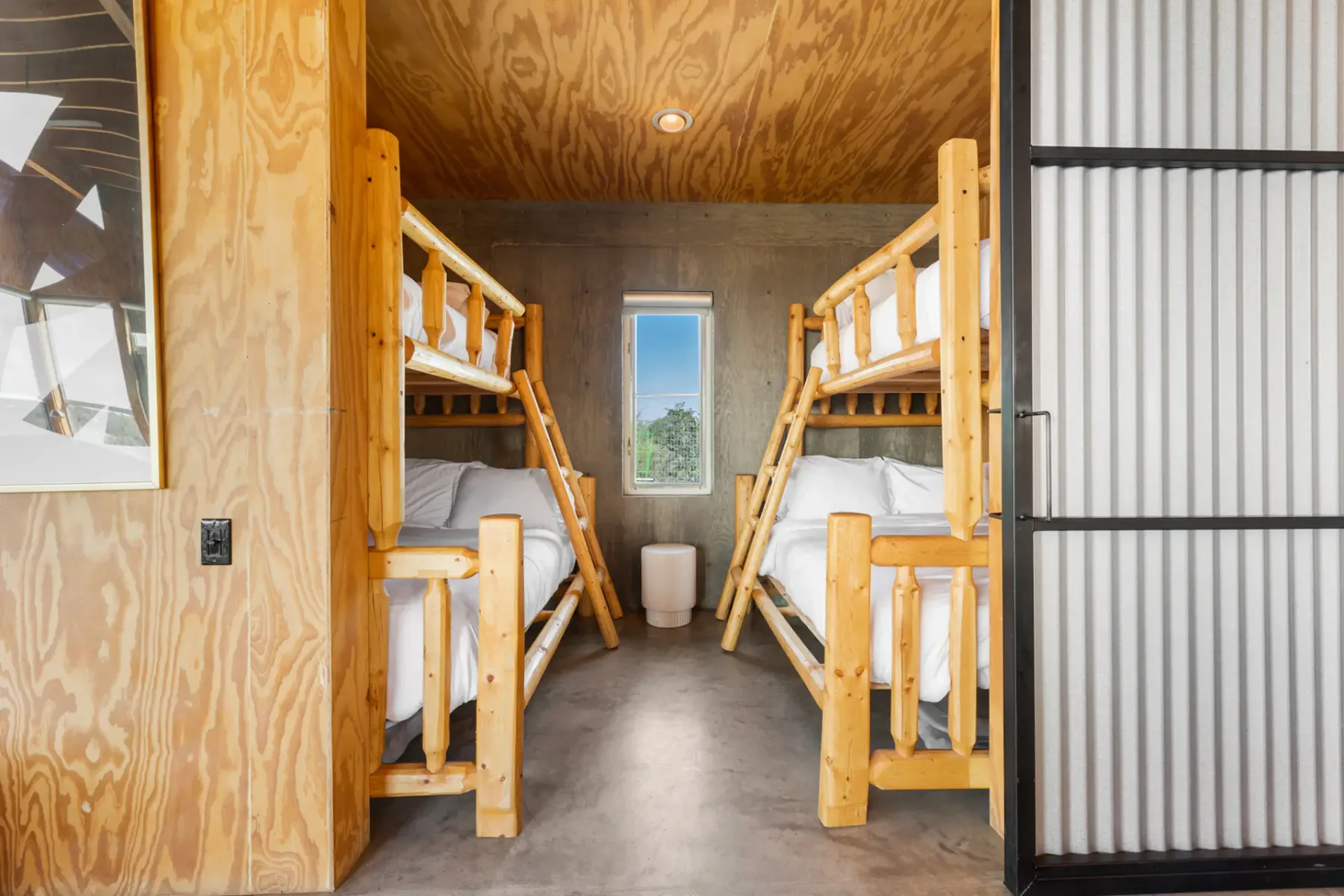 Room with two wooden bunk beds, small central window, and a corrugated sliding door, highlighting a minimalist design with natural light.