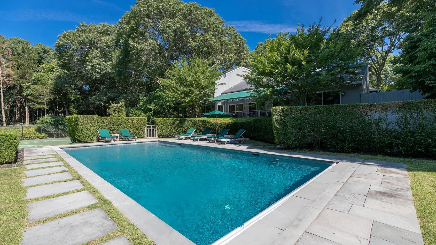 Una piscina al aire libre junto a una terraza pavimentada y vegetación frondosa.