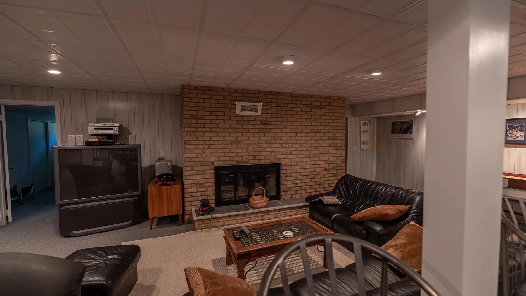 Una sala en el sótano con chimenea de ladrillo, televisor y asientos.