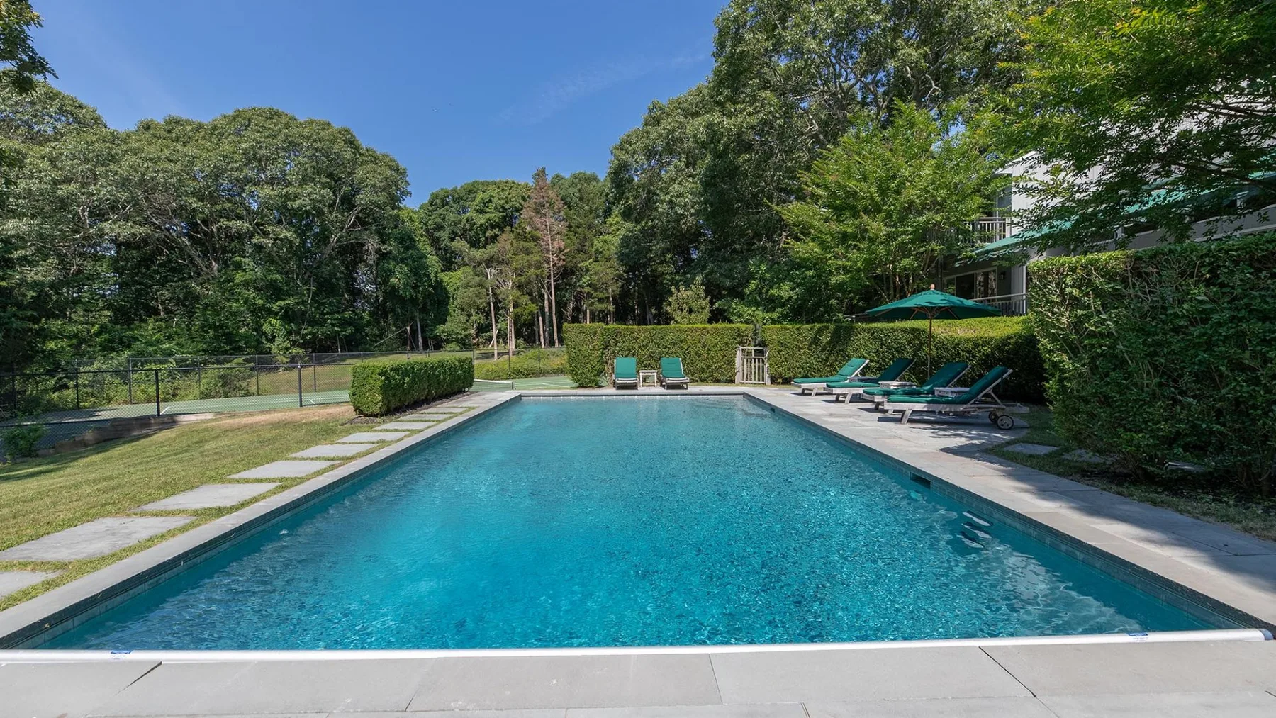 Una piscina al aire libre está rodeada de árboles y asientos junto a la piscina.