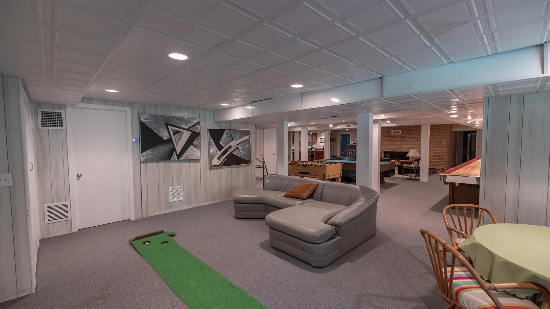 Una sala en el sótano con asientos seccionales y un pequeño putting green.