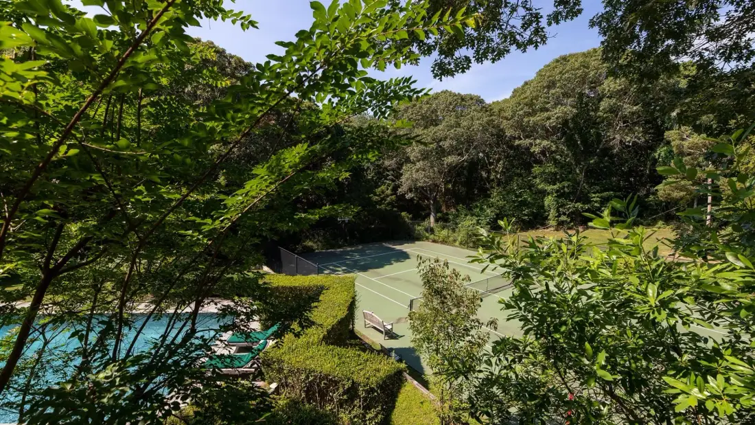 Una cancha de tenis y una piscina están rodeadas de árboles y vegetación.