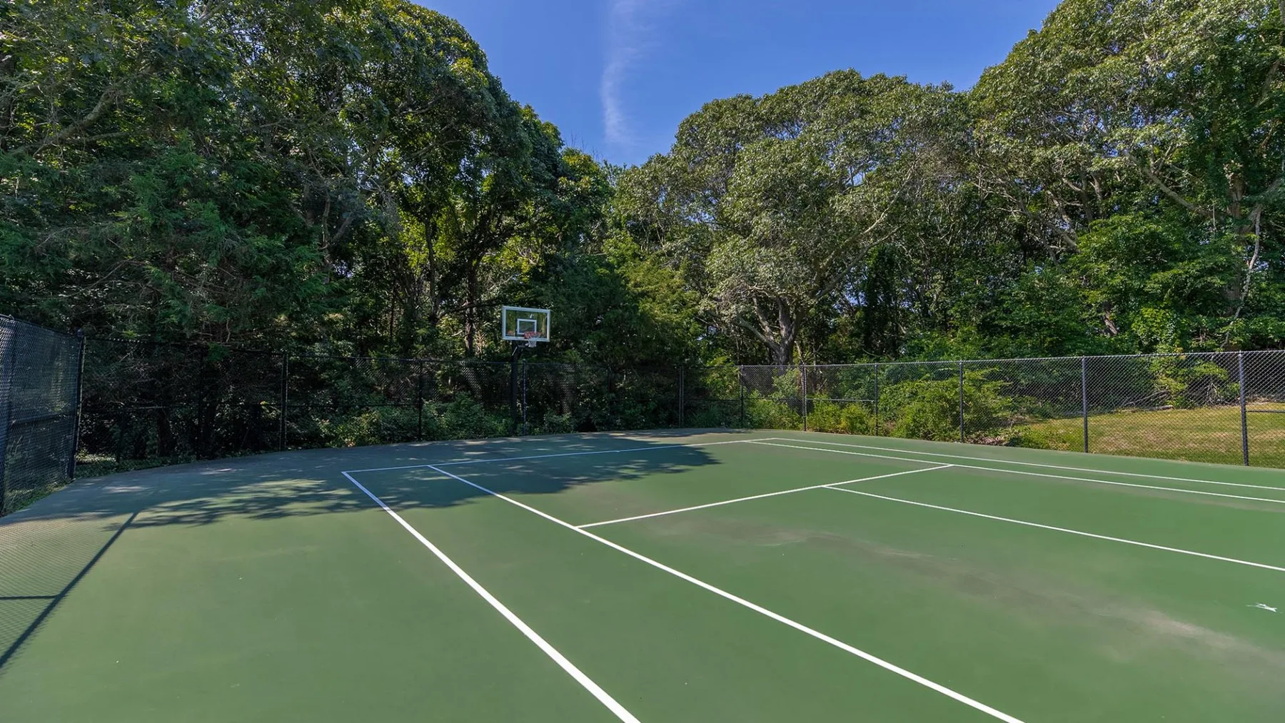 Una cancha verde al aire libre con líneas blancas está rodeada de árboles.