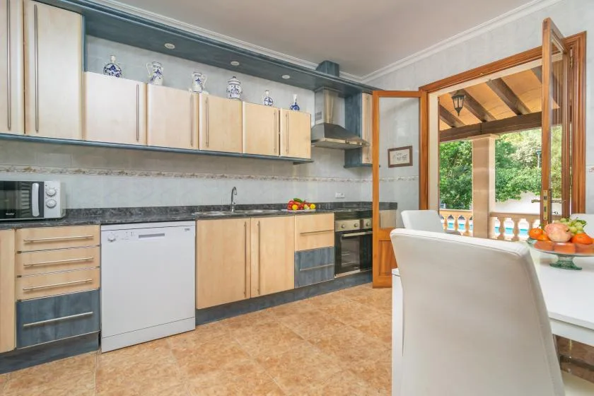 A bright kitchen with pale cabinets and a dining table beside open windows.