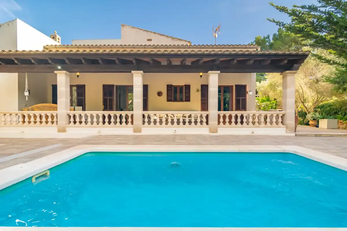 A swimming pool in front of a house with a covered veranda.