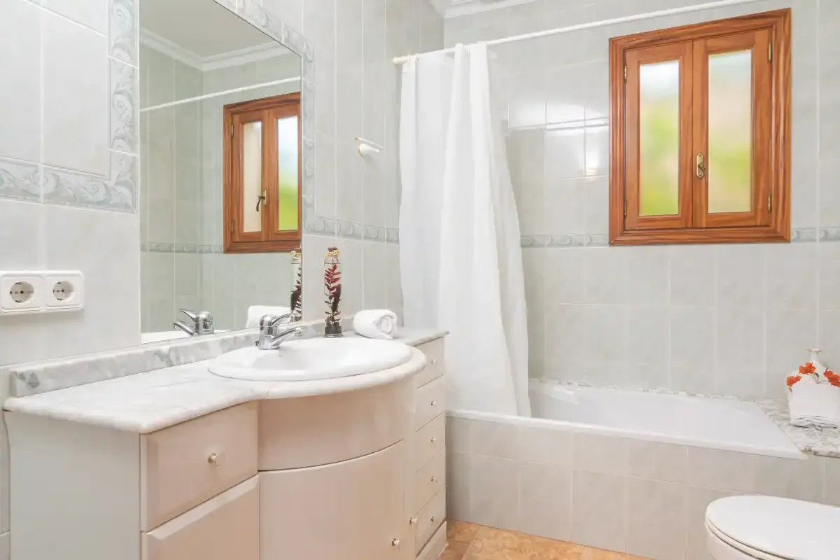 A tiled bathroom has a sink vanity, bathtub, and wood-framed window.