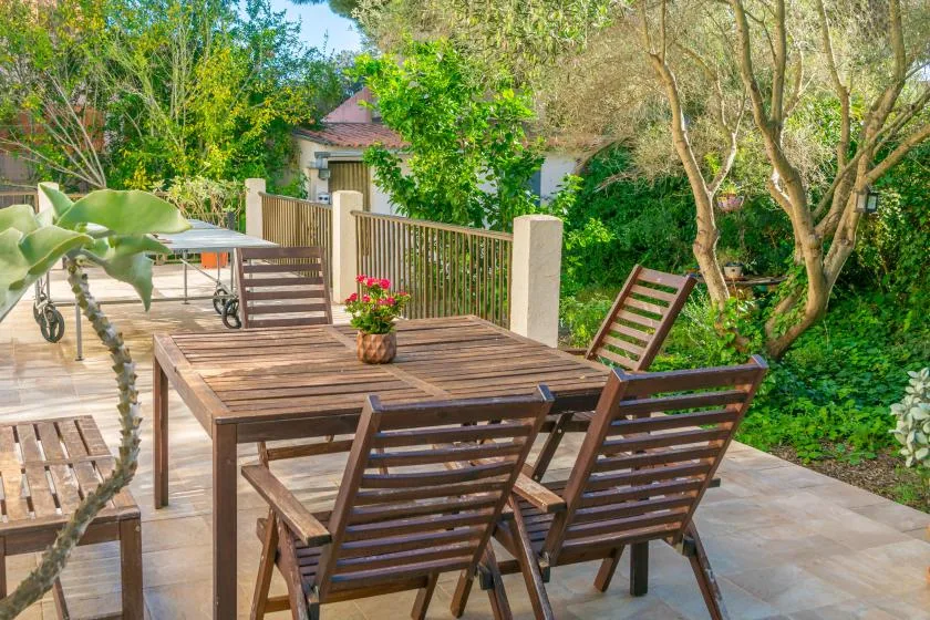 An outdoor dining area with a wooden table and chairs surrounded by greenery.