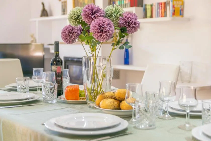 A dining table is set with dishes and glasses, with flowers in a vase at the center.