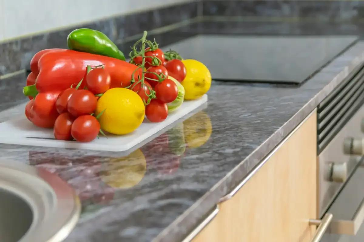 A kitchen countertop displays fresh tomatoes, peppers, and lemons beside the sink.