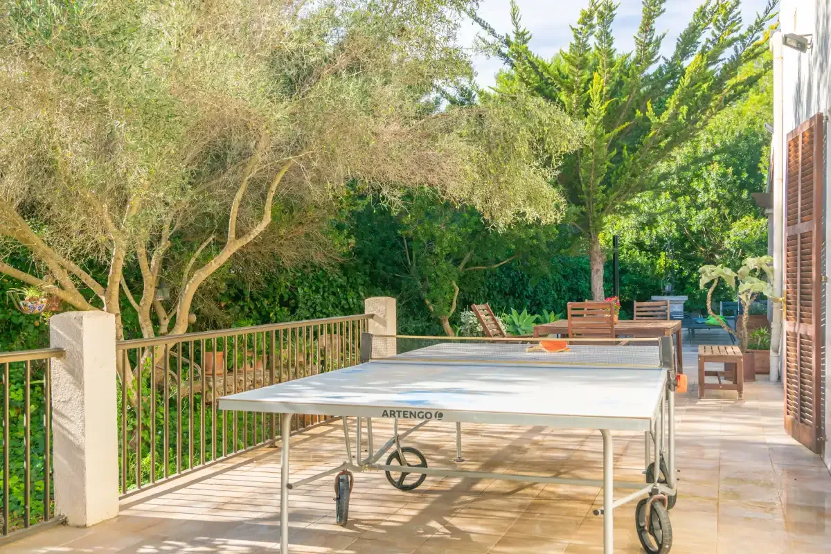 An outdoor table tennis area sits beside a paved patio surrounded by trees.
