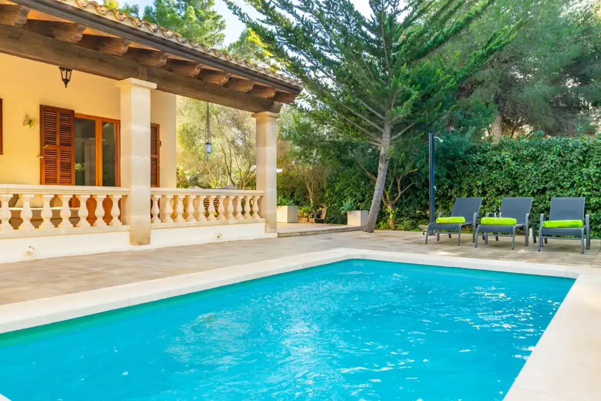 An outdoor swimming pool beside a covered patio and garden seating.