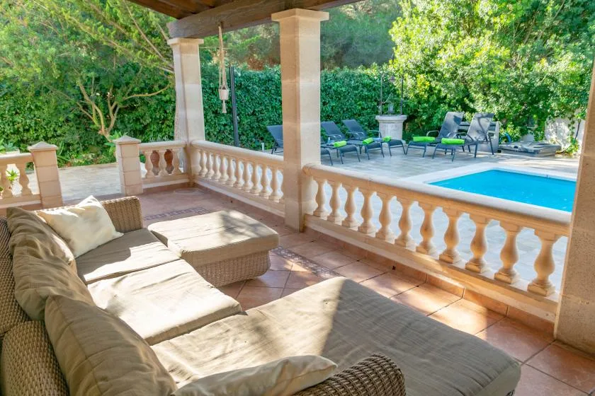 A covered outdoor seating area overlooks a swimming pool and green garden.