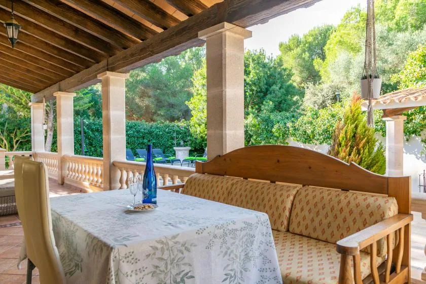 A covered outdoor dining area has a patterned tablecloth and cushioned bench seating.