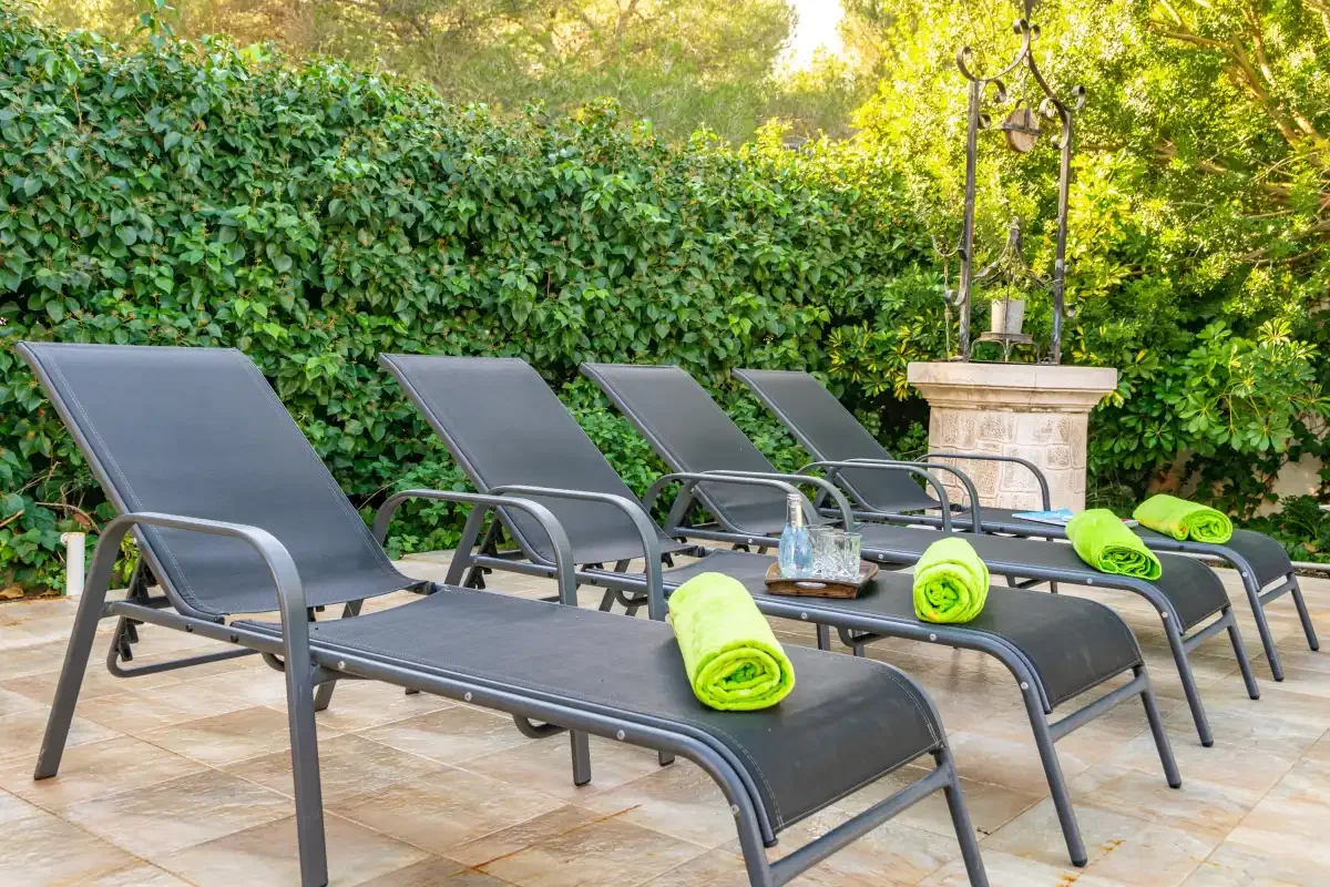 Outdoor poolside seating with lounge chairs and green towels on a tiled patio.