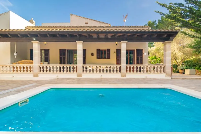 A swimming pool sits in front of a covered patio with columns.