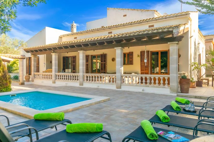 A swimming pool and loungers sit in front of a covered patio.