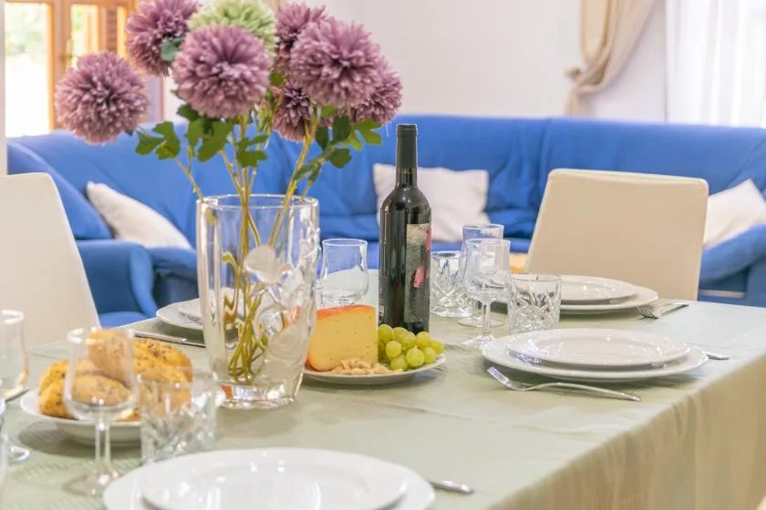 A dining table is set with dishes, glasses, and flowers in front of blue seating.