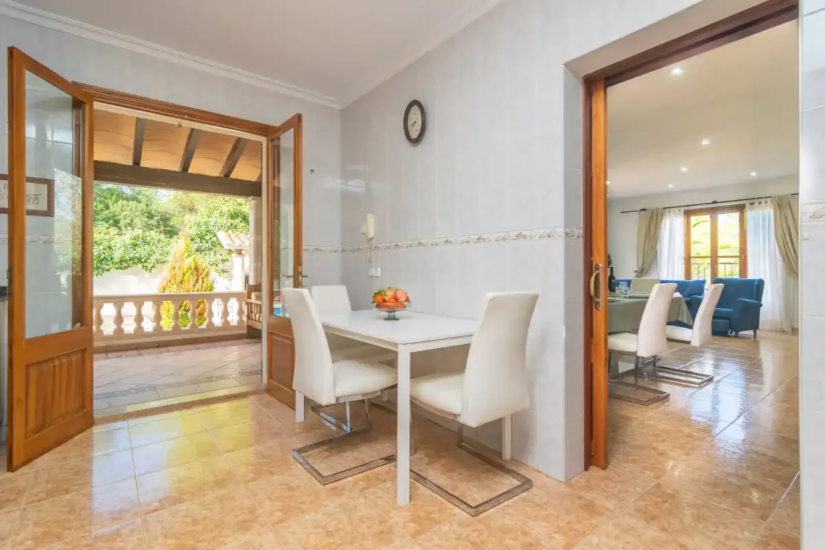 A dining area with a white table and chairs opens onto a balcony and adjoining sitting room.