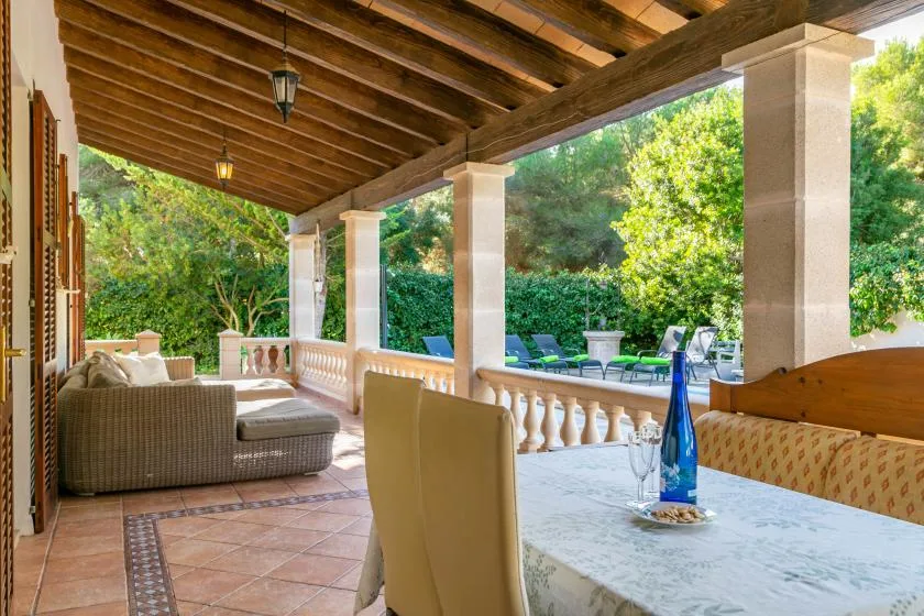 A covered patio with outdoor seating and a table overlooks a leafy garden.