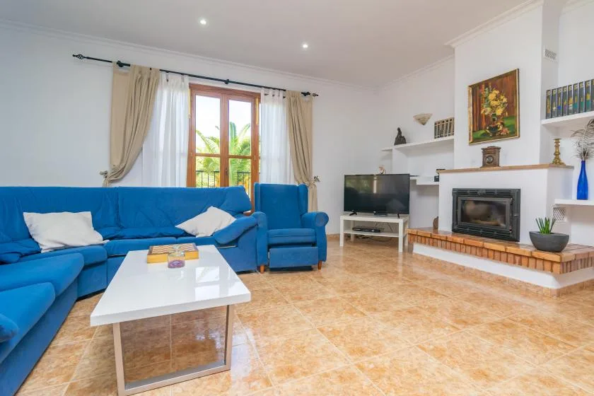A bright living room with blue seating, a television, and a fireplace.