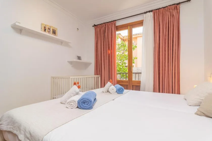 A bedroom with two beds, folded towels, and a window framed by curtains.