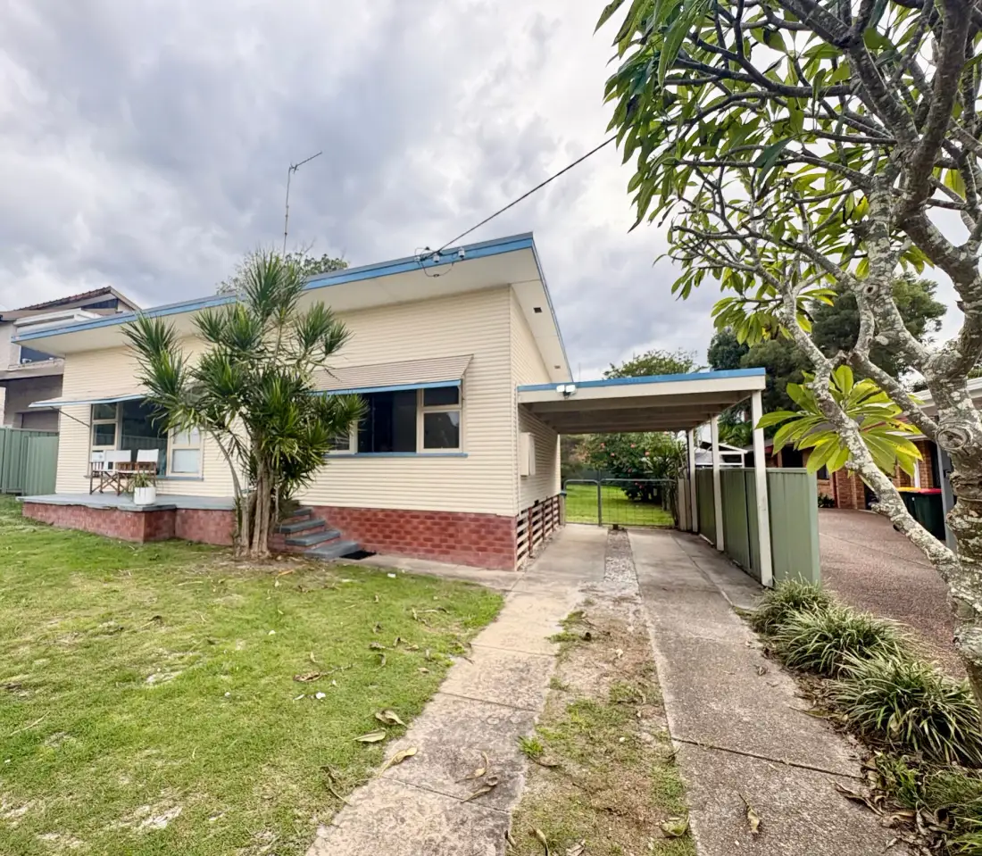 Exterior view of a low house with a driveway and carport.