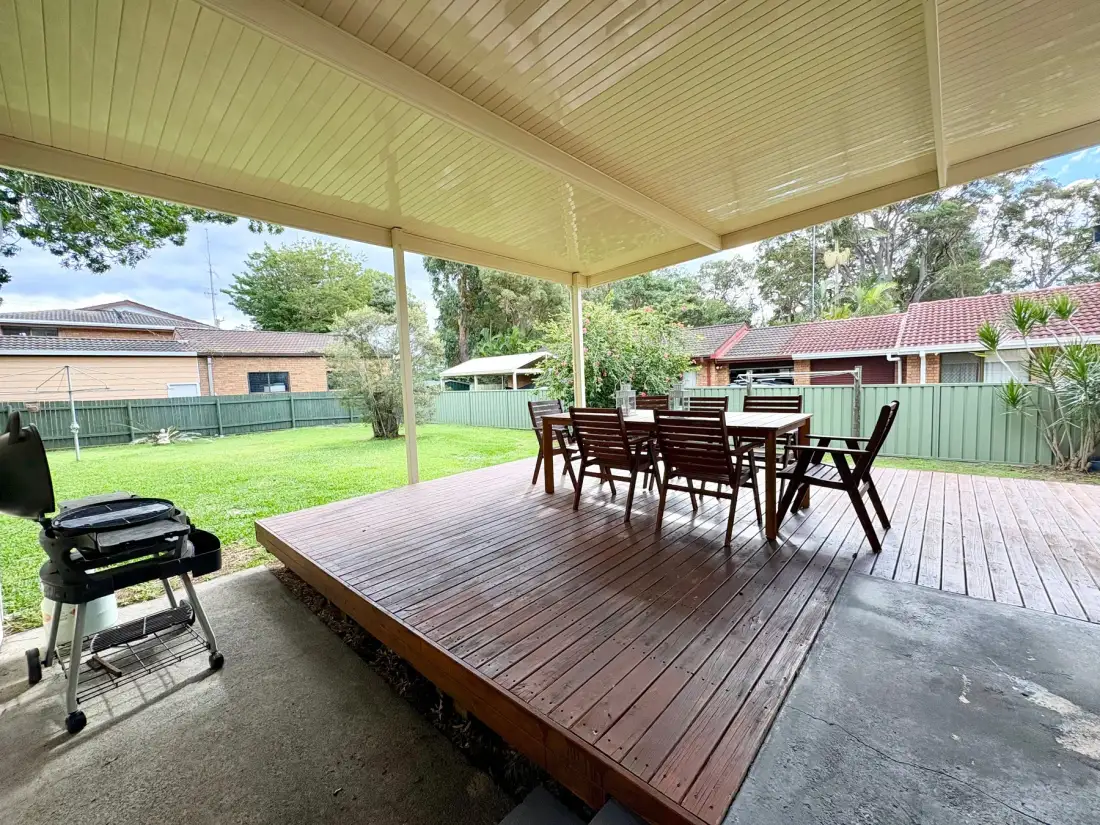 Covered outdoor dining area with a wooden table and chairs overlooking a lawn.