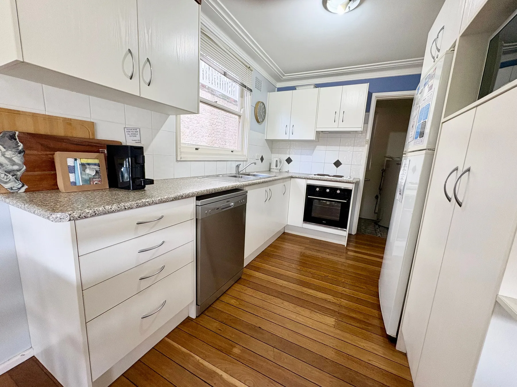 A bright kitchen with white cabinets, countertops, and a wooden floor.