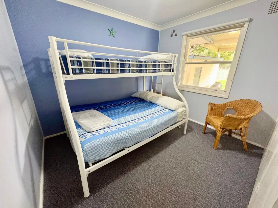A bedroom with a white bunk bed, blue bedding, and a wicker chair.