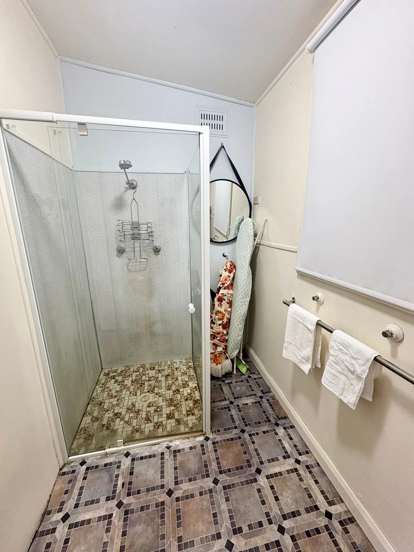A bathroom with a glass shower and patterned tile flooring.