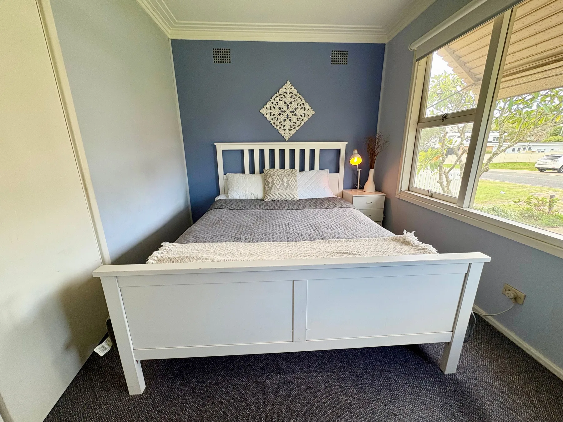 A bedroom with a white bed facing a blue accent wall and a large window.
