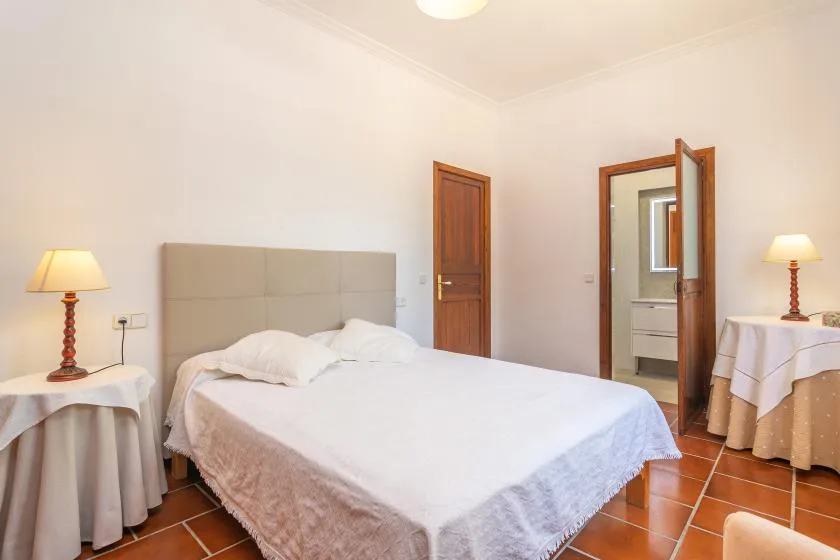 Un dormitorio con una cama doble, mesas auxiliares y una puerta hacia otra habitación.