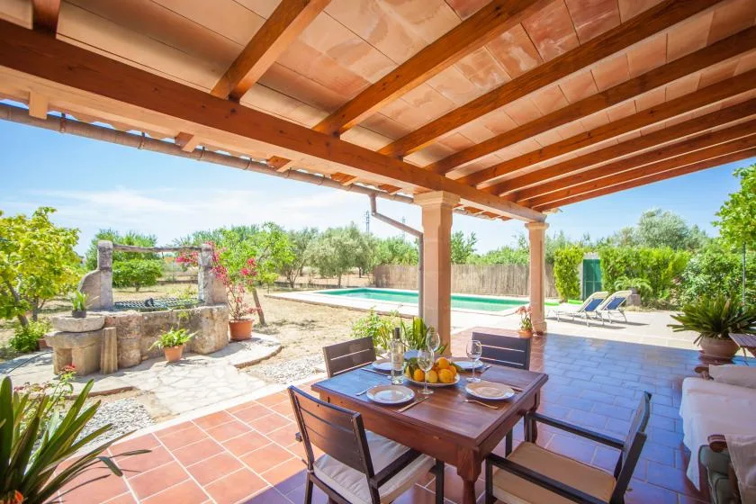 Un comedor exterior cubierto da a una piscina y un jardín con plantas.