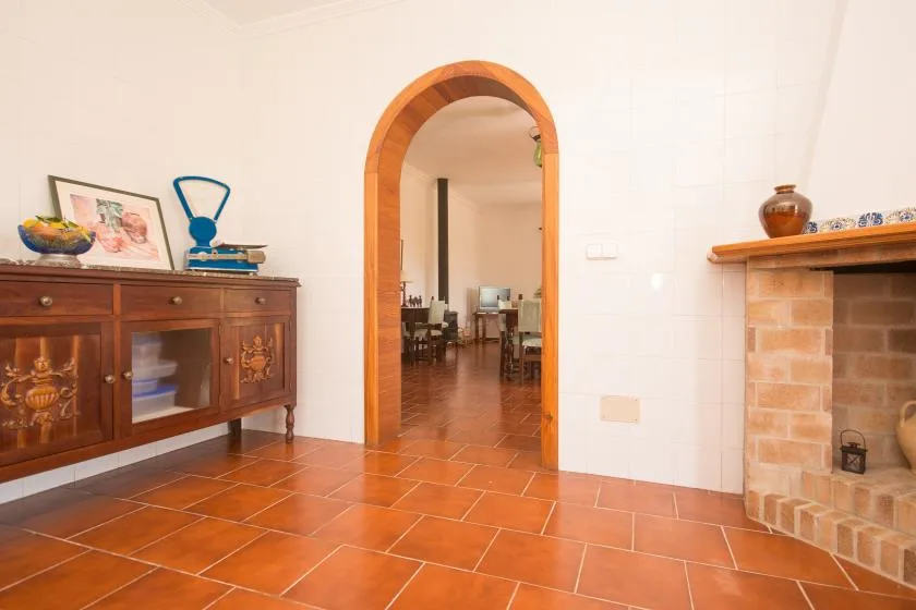 Una sala con suelo de baldosas, un aparador de madera y una puerta arqueada.