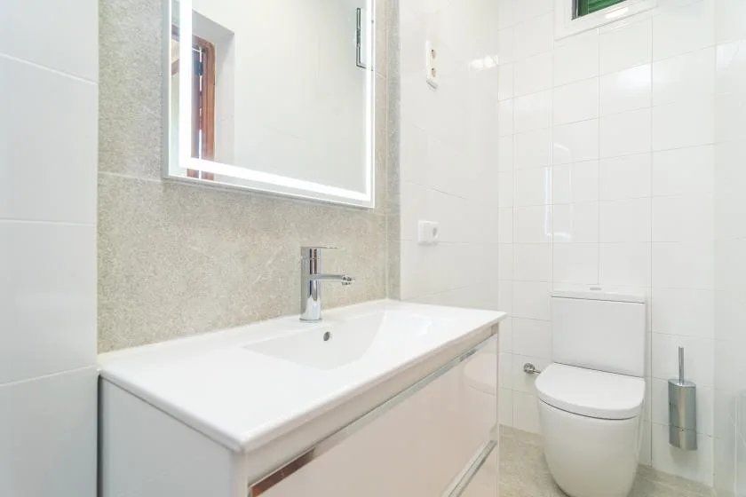 Un baño luminoso con lavabo, espejo e inodoro.